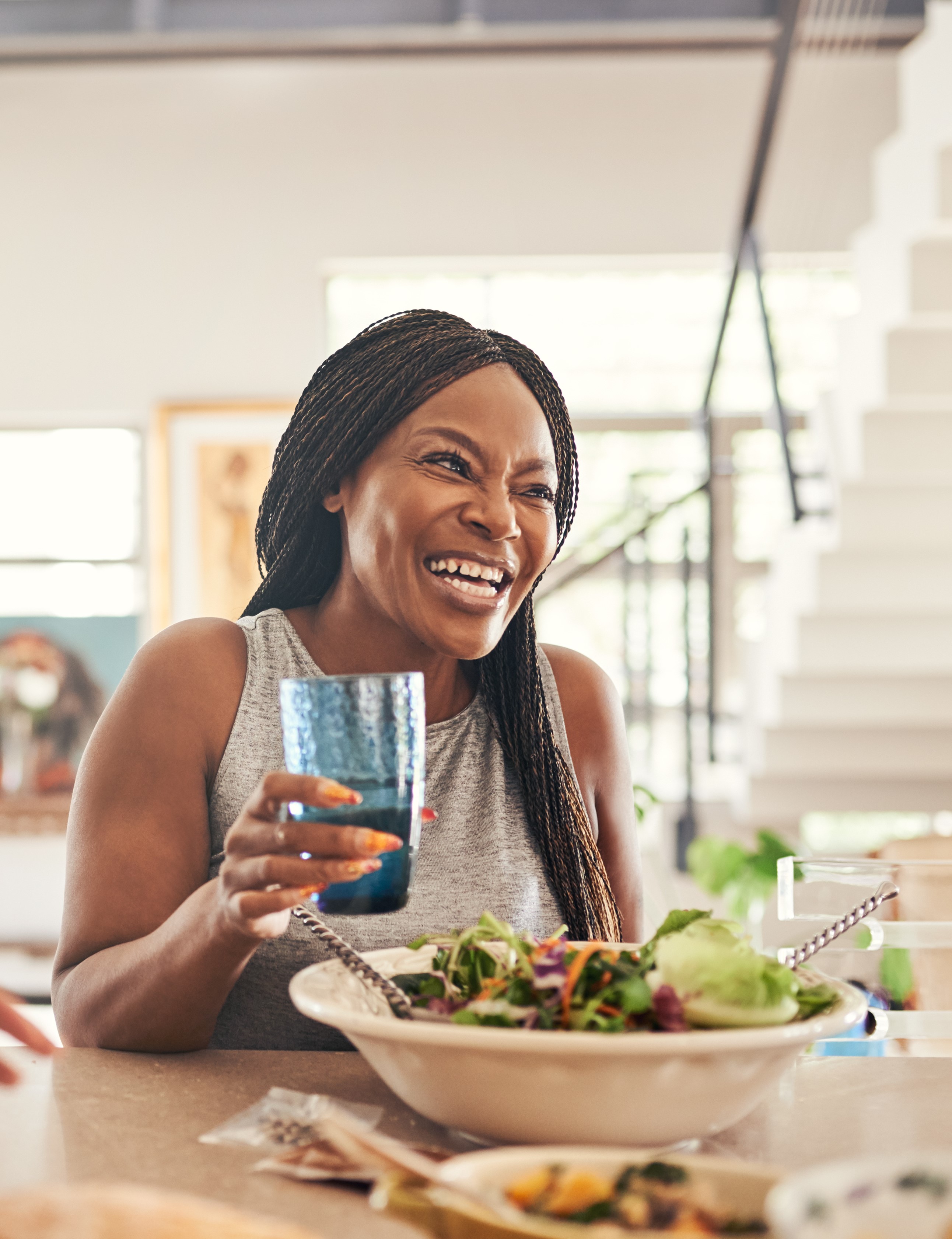African American woman holding a glass of water with a salad on the table.