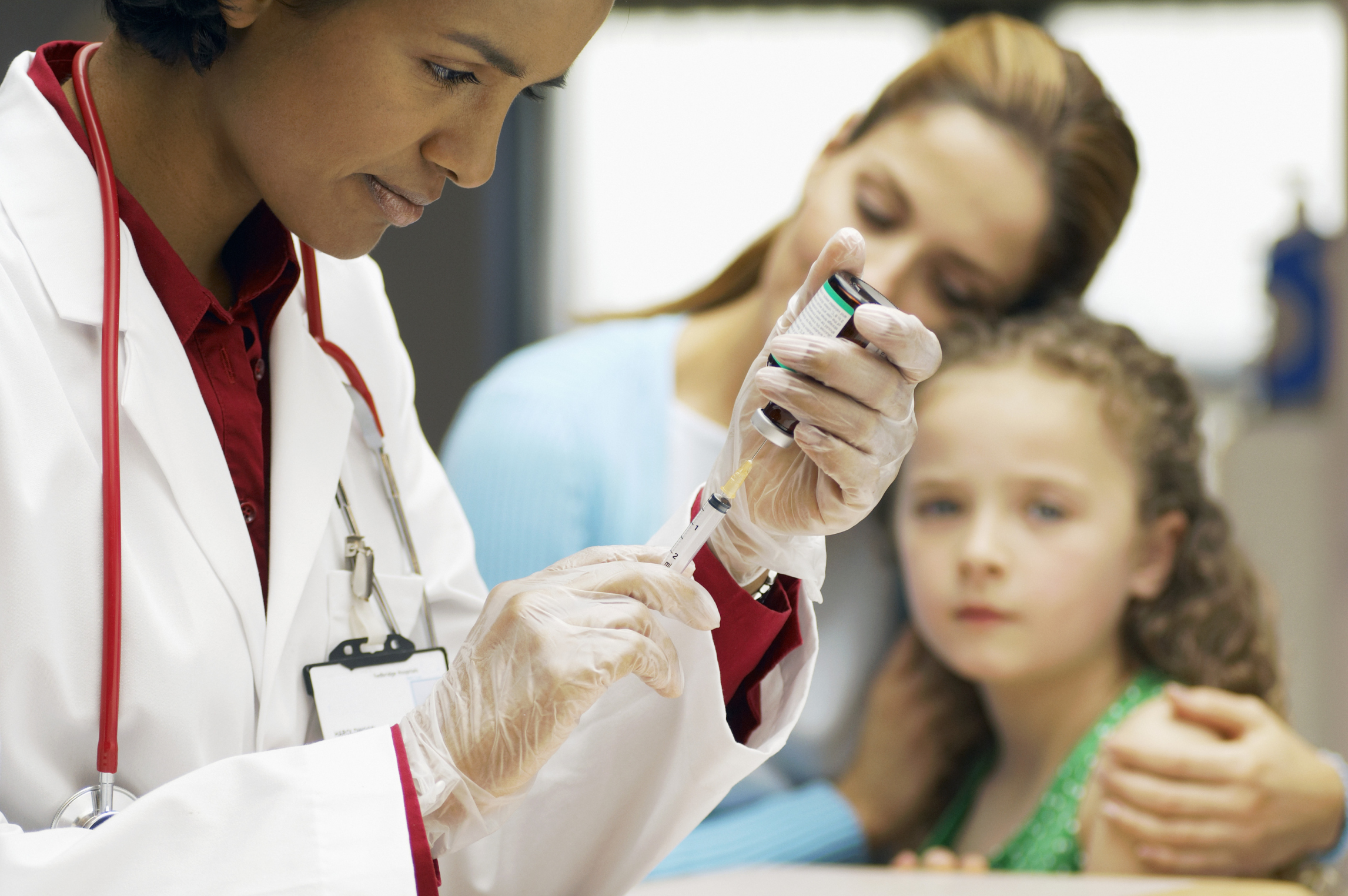 Picture of a provider drawing up a vaccine from a vial with a mother and child sitting in the background