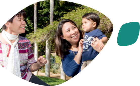 A smiling Asian mother holds her toddler facing his smiling grandmother